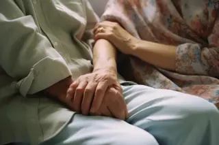 Duas pessoas idosas de mãos dadas, mãos apoiadas sobre as pernas, com roupas claras e estampa floral