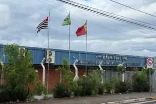 Fachada da Prefeitura Municipal de Barretos com três mastros de bandeiras, cerca e calçada em primeiro plano