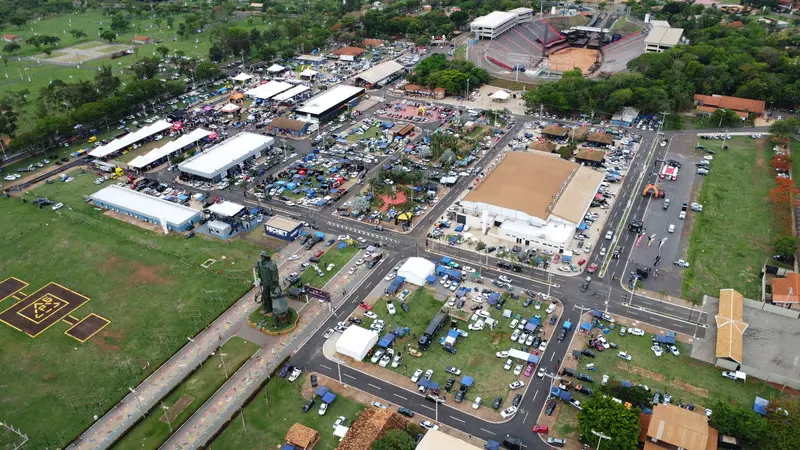 Vista aérea do Parque do Peão em Barretos com estandes, tendas, veículos e a arena ao fundo