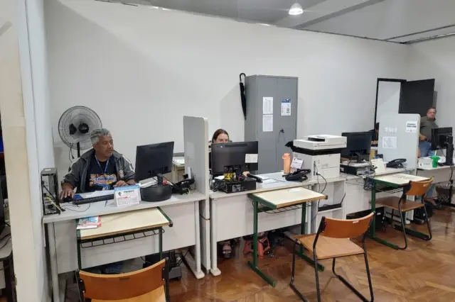 sala de atendimento com balcões, computadores e atendentes sentados